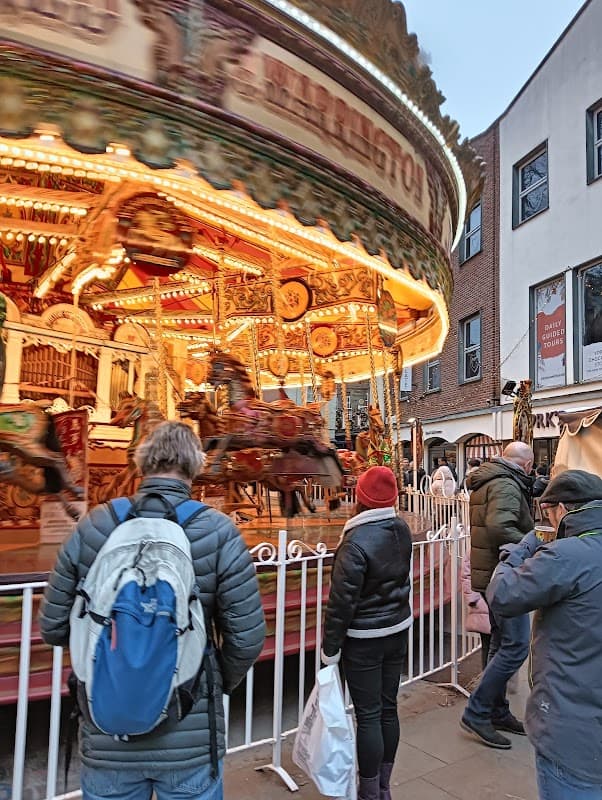 Colorful carousel with lights, people watching, and historic buildings in a lively street scene in York.
